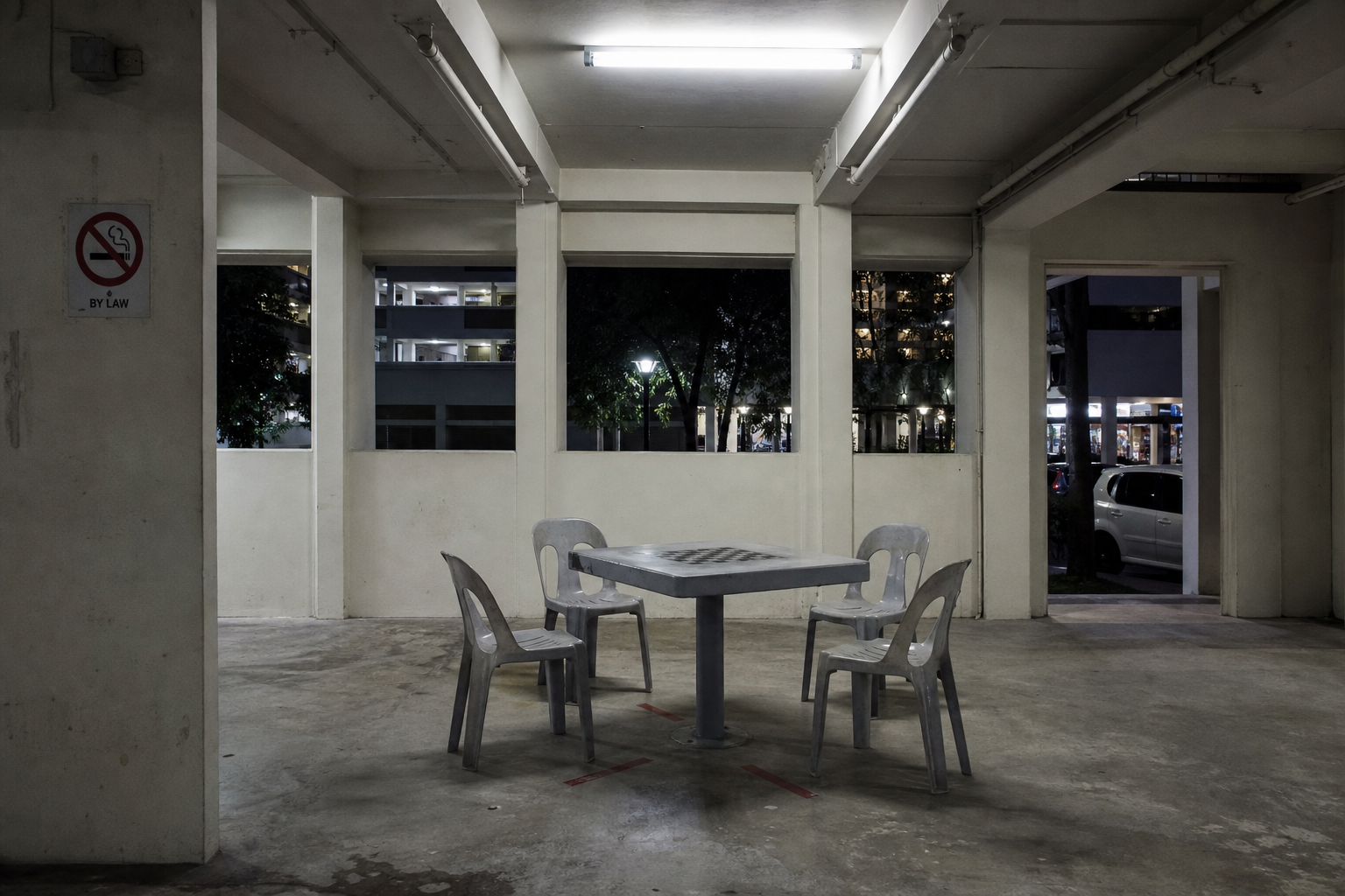 Void-deck plastic chairs around the chess table under fluorescent light