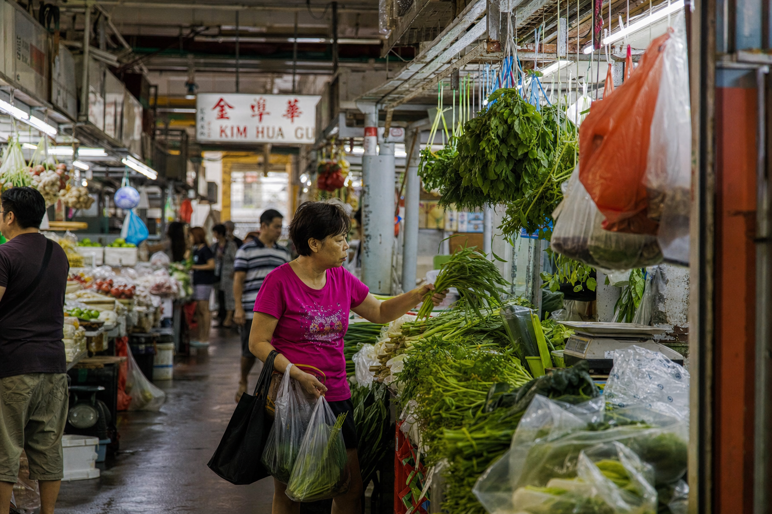 Chinatown Complex wet market aisle with hanging greens under fluorescent light